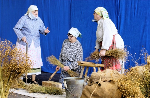 Trzy kobiety w stroju wiejskim przy pracy, obok snopki, zioła