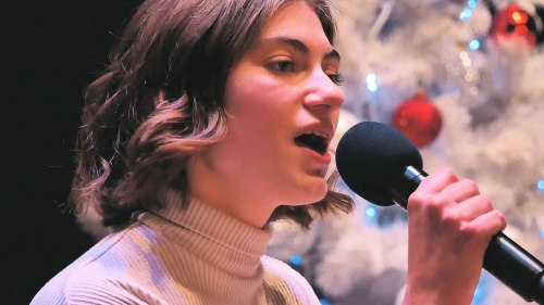 Aleksandra Bragiel śpiewa do mikrofonu w tle w rozmyciu - głębia ostrości zdjęcia - widać ozdoby świąteczne