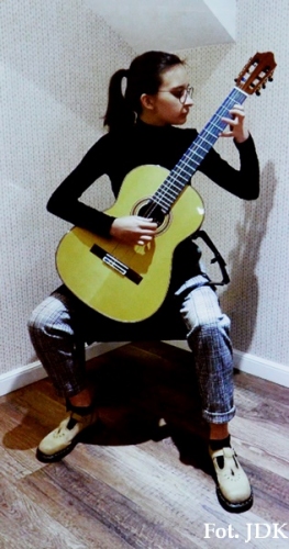 Młoda kobieta w jeansowych spodniach gra na gitarze akustycznej koloru żółtego