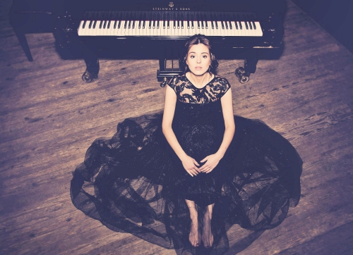 Pianistka w czarnej sukni siedzi na podłodze za nią duży fortepian