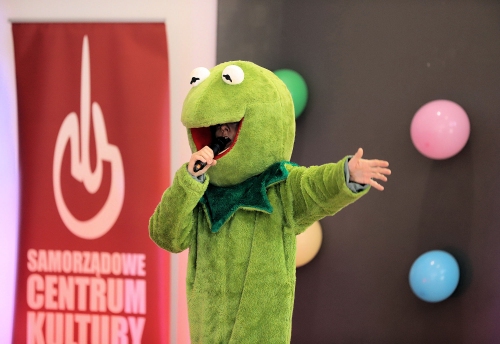 Animator przebrany za Kermita żabę trzyma wyciągniętą prawą rękę