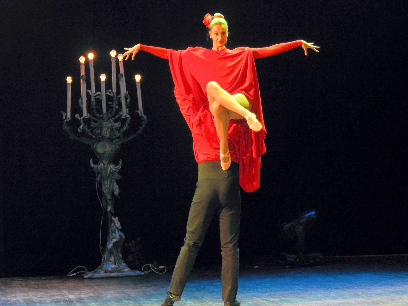 Tancerka w czerwonej kreacji wysoko uniesiona przez partnera ubranego na czarno.