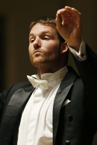 Jiři Petrdlik – dyrygent, ubrany w czarny frak i białą koszulę z batutą w ręku dyryguje orkiestrą