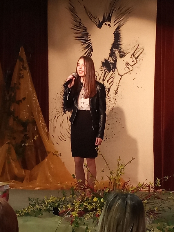 Na tle loga konkursu czyli gołębicy unoszącej się do nieba śpiewa, stojąc na scenie Weronika Dębska