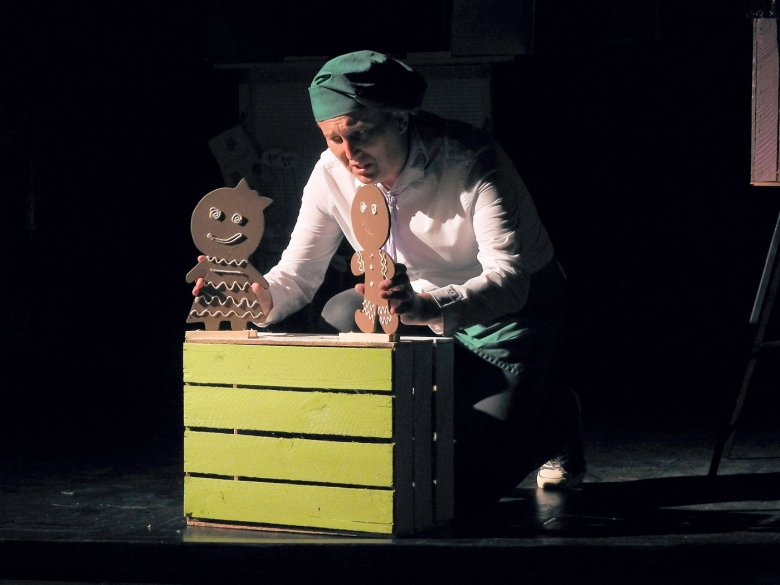 Na scenie aktor, który animuje dwie kukiełki, ciastek piernikowy i jego żeński odpowiednik