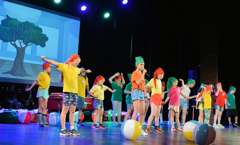 Dzieci ubrane w kolorowe ubrania stoją na scenie w trakcie spektaklu