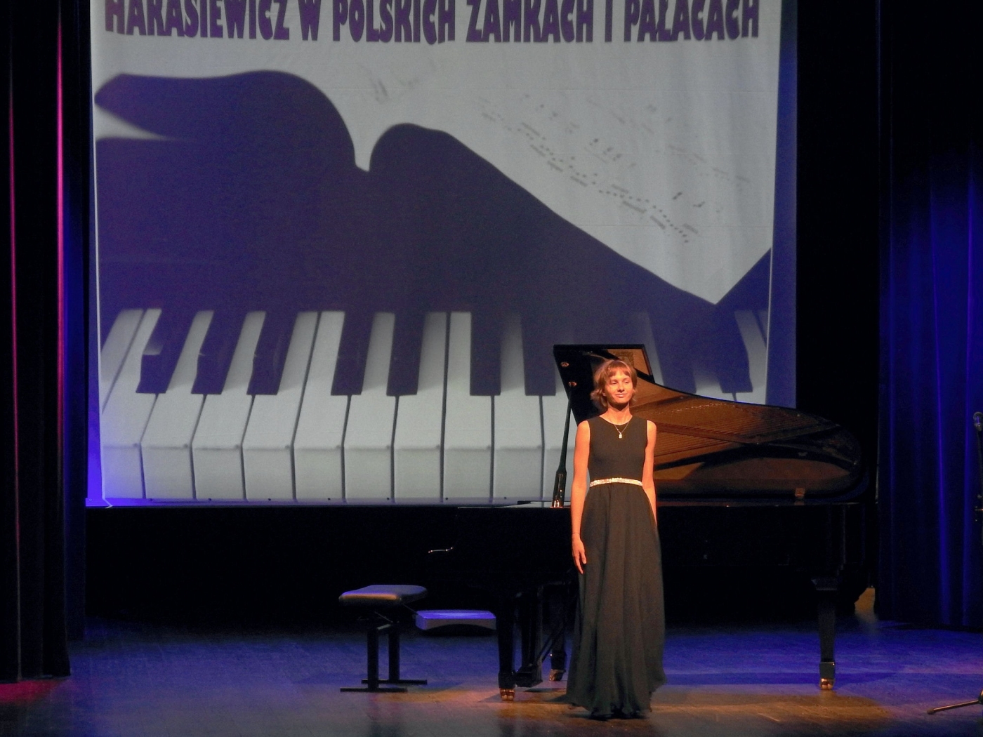 Dziewczyna stoi na scenie przodem do widowni - prezentuje się przed grą na fortepianie