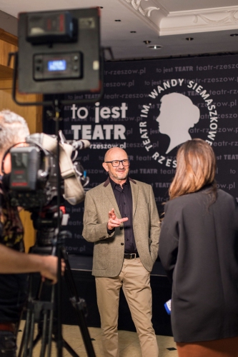 Dyrektor Teatru Jan Nawara udziela wywiadu do telewizji w tle widać kamerę na statywie oraz dziennikarkę z mikrofonem