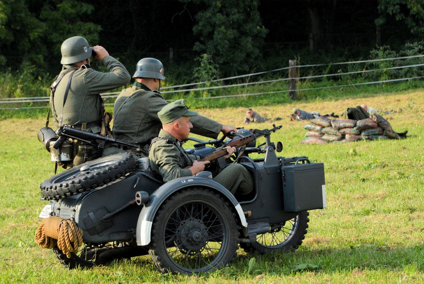 Motocykl wojskowy na nim trzech żołnierzy - jadą przez pole.