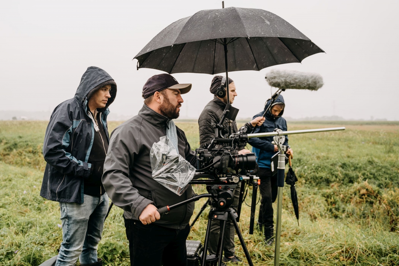 Ekipa filmowa w plenerze podczas kręcenia filmu. Pada deszcz widać czarne parasole.