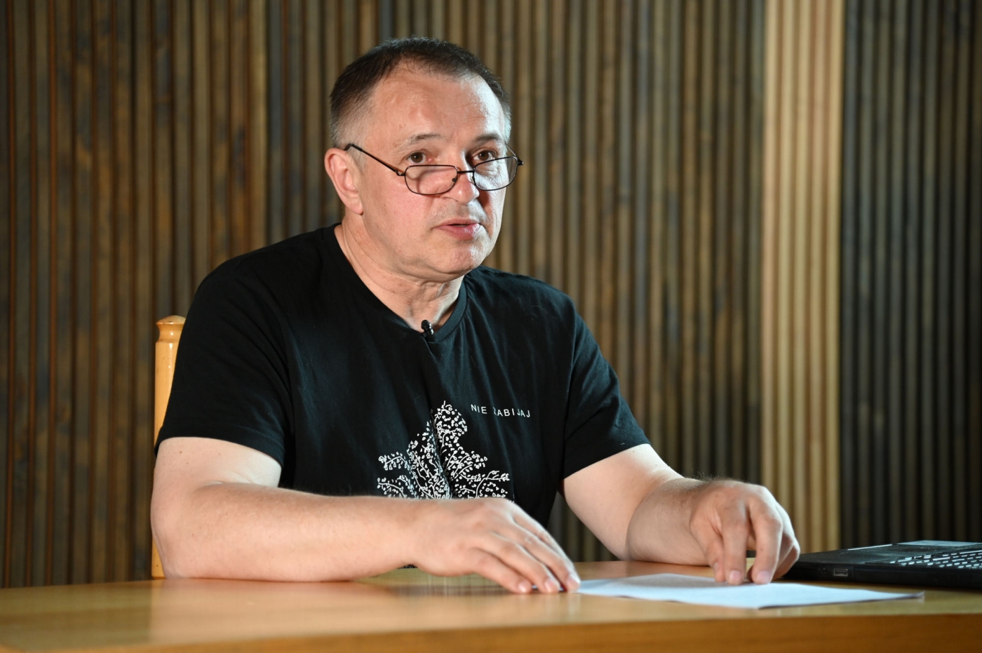 Wojciech Birek w czarnym t-shircie przy biurku podczas wykładu
