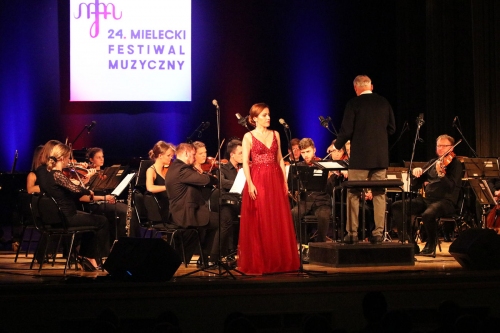 Śpiewająca pani w czerwonej sukni w tle zespół smyczkowy gra podczas koncertu finałowego