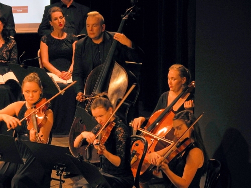 Część zespołu w czasie koncertu pulpity z nutami kilku skrzypków oraz wiolonczela