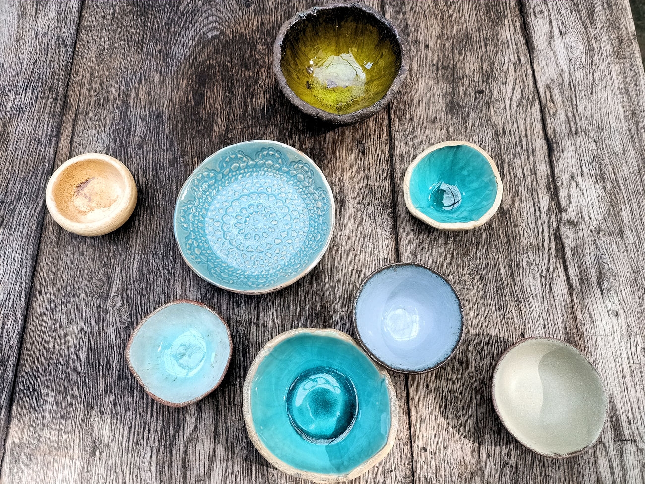 Na drewnianym stole leżą wykonane własnoręcznie różne kolorowe naczynia ceramiczne