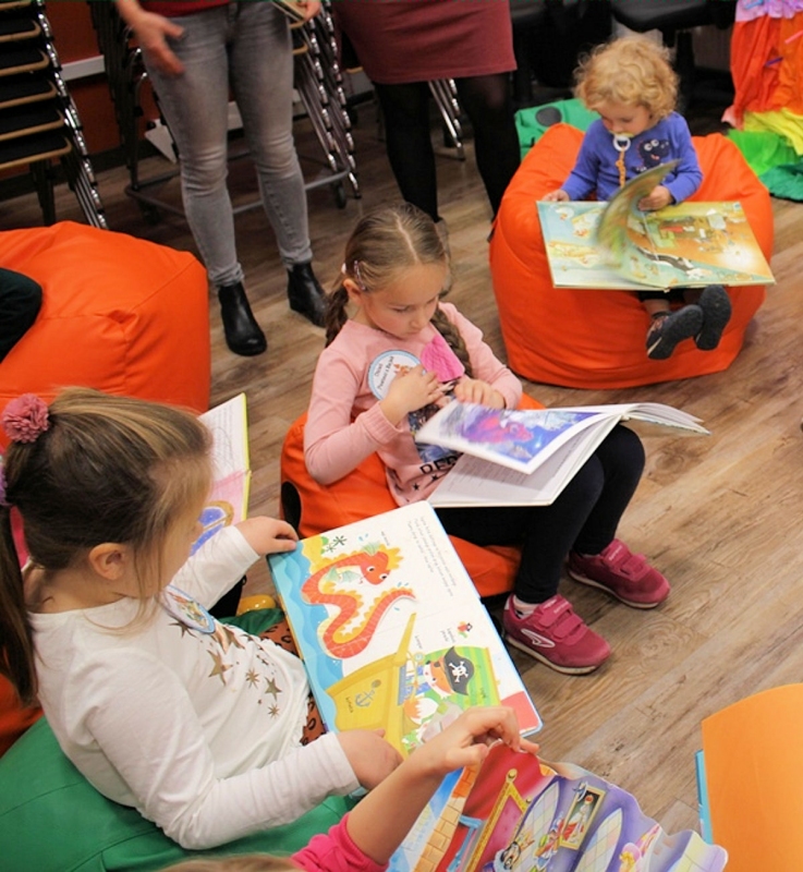 Dzieci siedzą na kolorowych pufach i czytają kolorowe bajki z ilustracjami