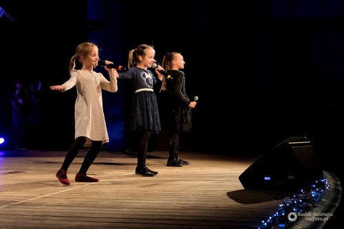 Trzy młode dziewczynki stoją na scenie i śpiewają w czasie koncertu.