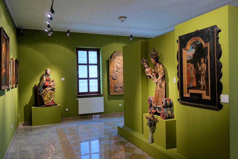 Sala sztuki sakralnej na ścianach wiszą obrazy, po prawej stronie widać figurę Matki Bożej trzymającej małego Jezusa