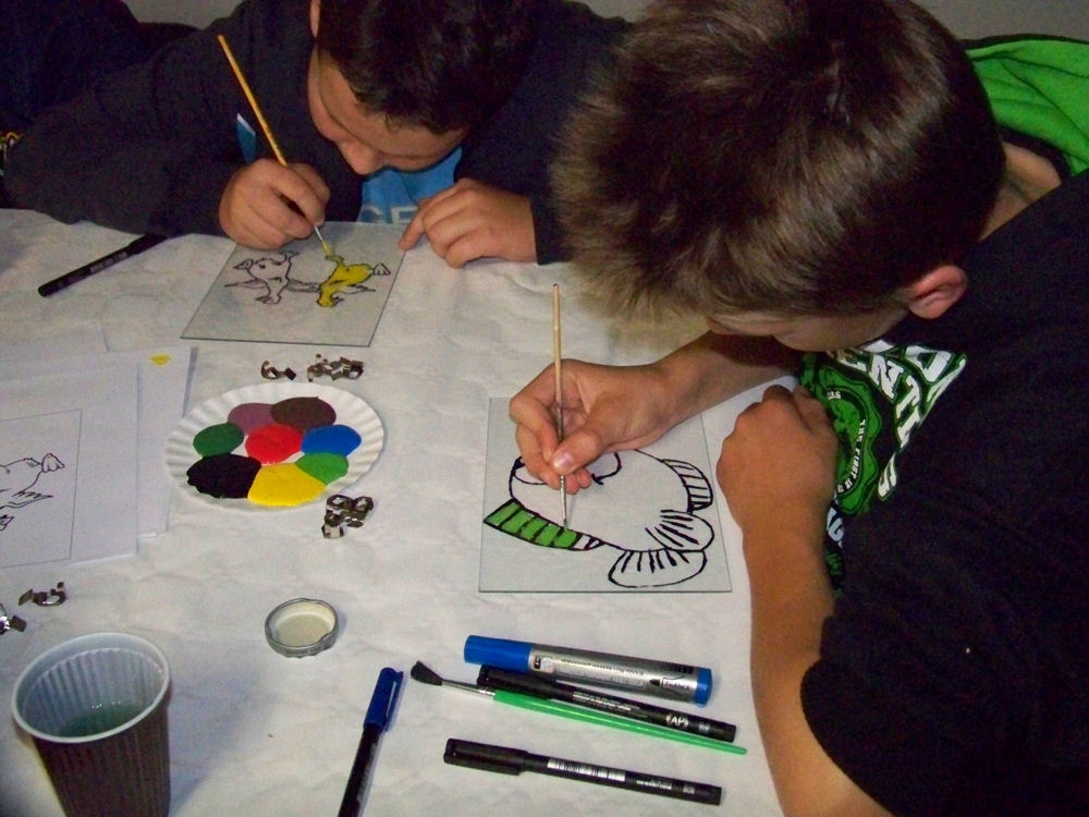 Dwójka chłopaków rysuje i maluje przy stoliku, na którym leżą kartki i inne przybory