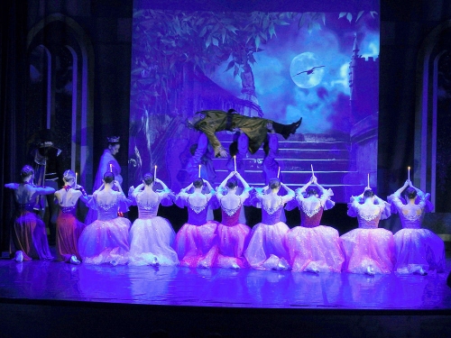 Na scenie klęczące baletnice nad głowami trzymają zapalone świeczki