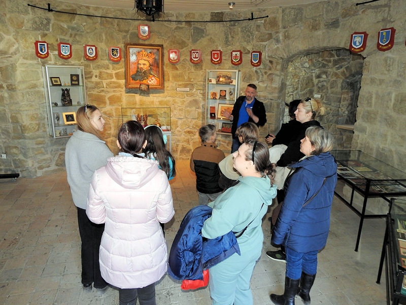 Oprowadzana grupa w sali na ścianach widać herby i popiersie Kazimierza Wielkiego