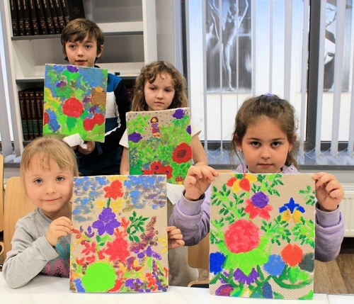 Dzieci trzymają w ręku namalowany w czasie zajęć prace - kolorowe kwiaty