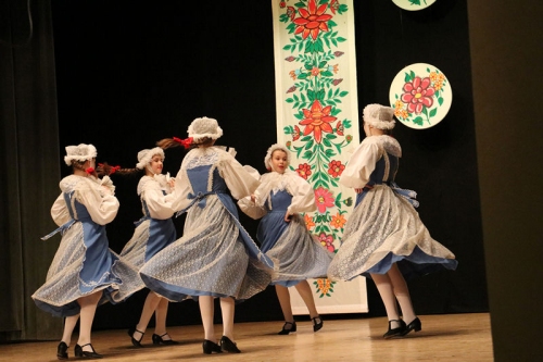 Dziewczyny w niebiesko białych spódnicach z białymi czepkami na głowie tańczą na scenie w trakcie koncertu