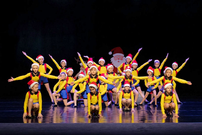 Tańczące dzieci na scenie w żółtych strojach i czapce świętego mikołaja