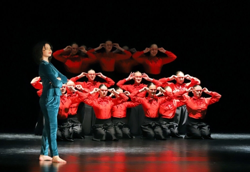 Młodzi tancerze w czerwono-czarnych strojach tańczą na scenie.