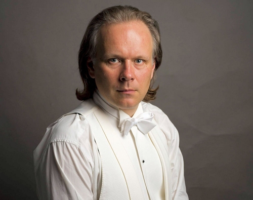 Zdjecie portretowe dyrygenta Piotra Kosa-Nowickiego w białej eleganckiej koszuli, białej kamizelce i białej muszce