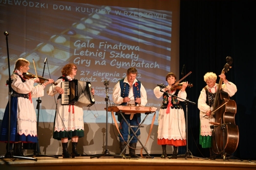Galeria przedstawia kilka zdjęć z koncertu w sali widowiskowej WDK. Na scenie widać grające na cymbałach dzieci ich nauczycieli oraz zespół Kurasie a także widownię