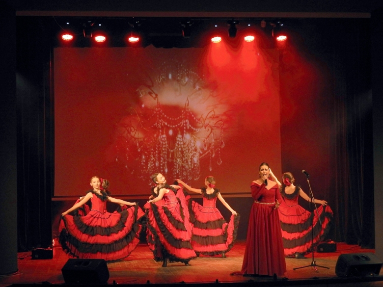 Kobiety w kolorowych sukniach tańczą w czasie koncertu na pierwszym planie śpiewająca artystka