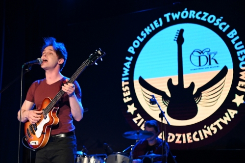 Muzyk uczestnik konkursu bluesowego śpiewa do mikrofonu i gra na gitarze w tle widać logo festiwalu z rzutnika
