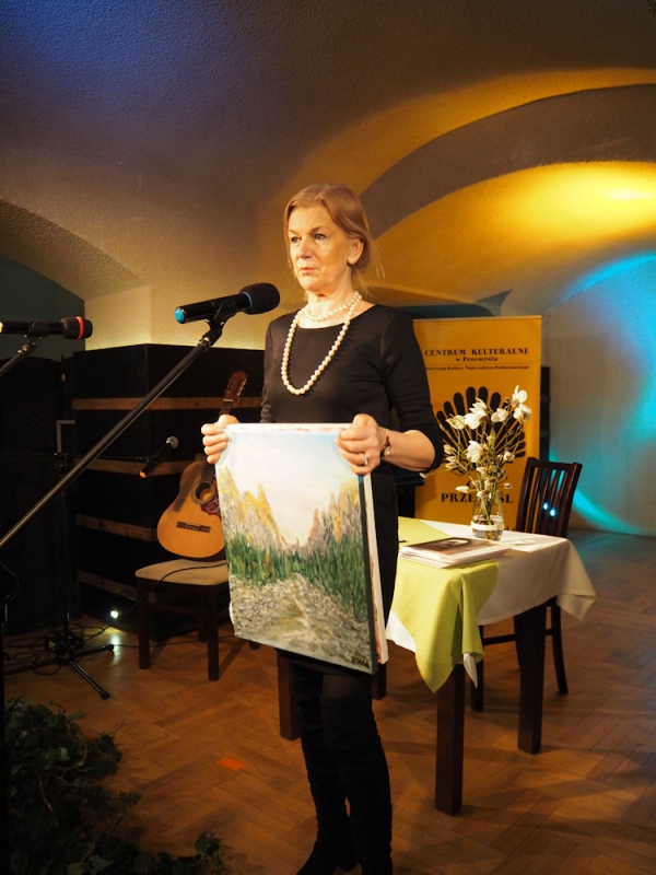 Krystyna Perlak prezentuje swój obraz pejzaż, który trzyma w ręce