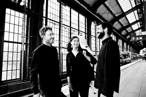 Czarno-białe zdjęcie trójki muzyków wykonane w jakiejś industrialnej hali