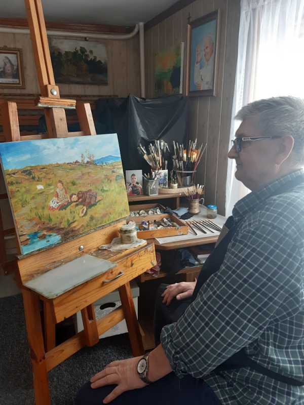 Artysta siedzi na krześle przed sztalugą na której jest namalowany obraz tego artysty